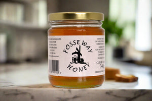 glass jar of amber colour runny honey with a gold lid and fosse way honey label.